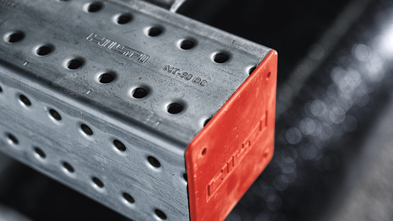 Nahaufnahme einer perforierten Hilti MT-90 OC Montageschiene aus verzinktem Stahl. Das offene Schienenende ist mit einer roten Schutzkappe versehen, während Hilti-Logo und Produktbezeichnung in die Metalloberfläche eingeprägt sind.