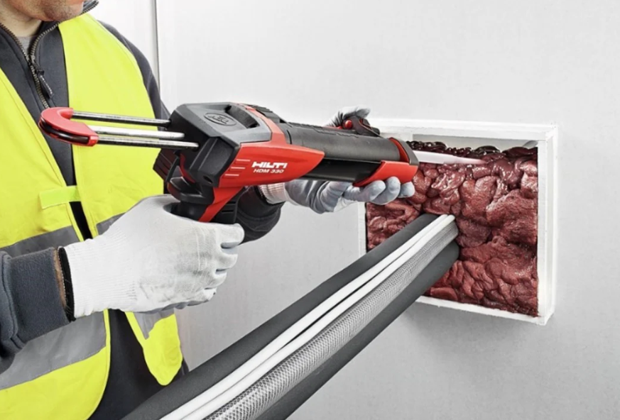 Two firestop cartridges with red-and-white �������� “Firestop” branding and hazard symbols beside clear protective safety goggles with black and red frames, set against a blurred industrial background.