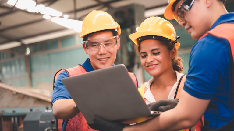 Three people wearing hard hats looking at a laptop