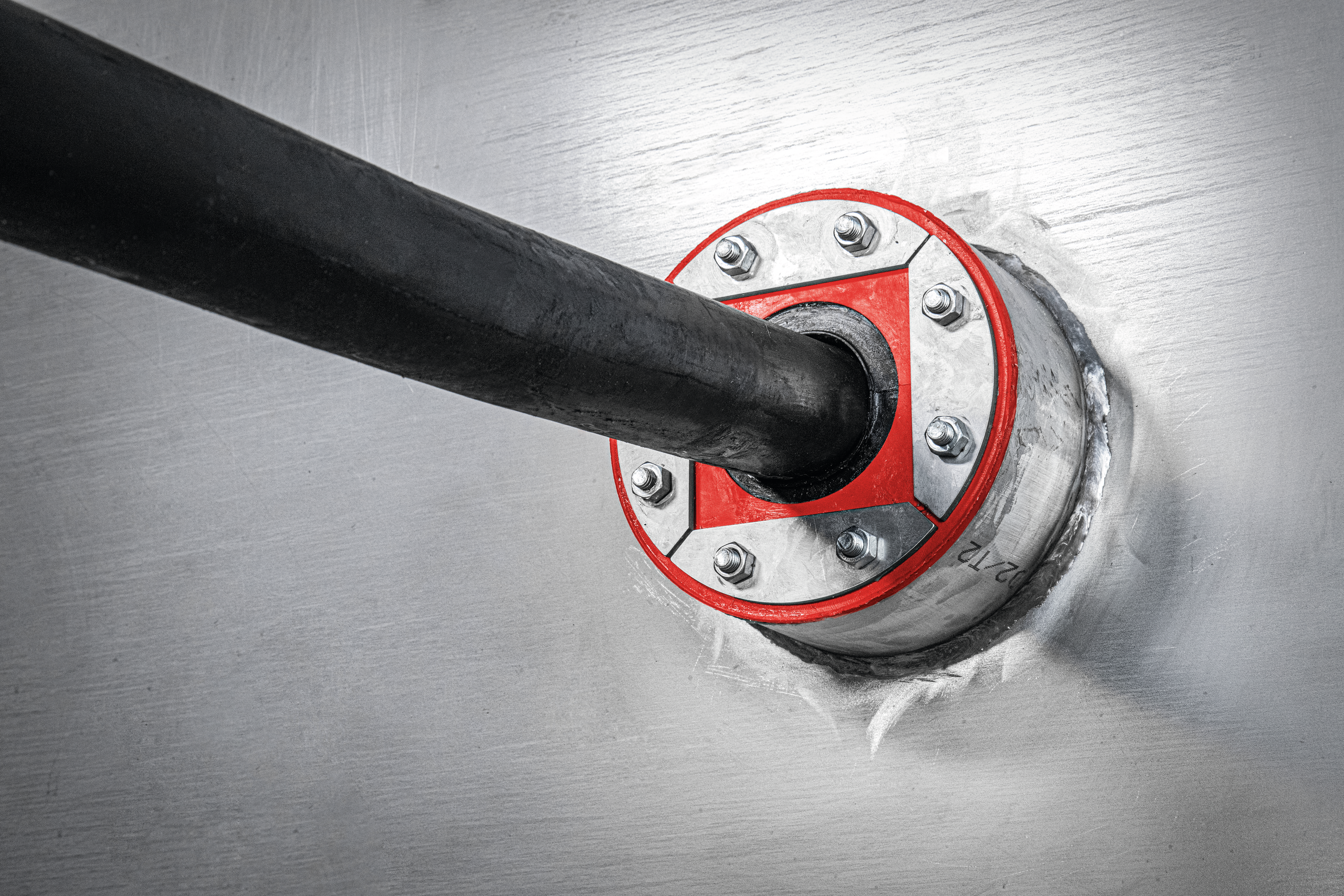 Pipe penetration sealed with a bolted metal transit frame and red firestop insert, creating a tight seal around a pipe passing through a wall.