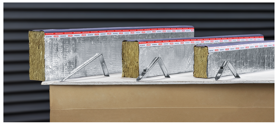 Foil-faced mineral wool cavity barriers on metal brackets, showing exposed insulation cores and staggered placement on a board, with a dark ribbed wall background.