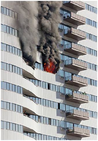High-rise apartment building with flames and heavy black smoke emerging from a mid-level unit, showing an active fire spreading from a balcony and window.