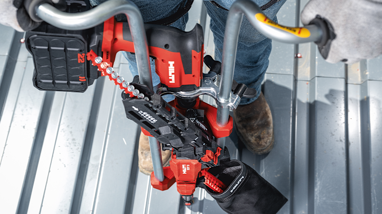 Application image of a worker installing screws on a metal roof deck, using the Nuron ST 2000-22 and SDT 9