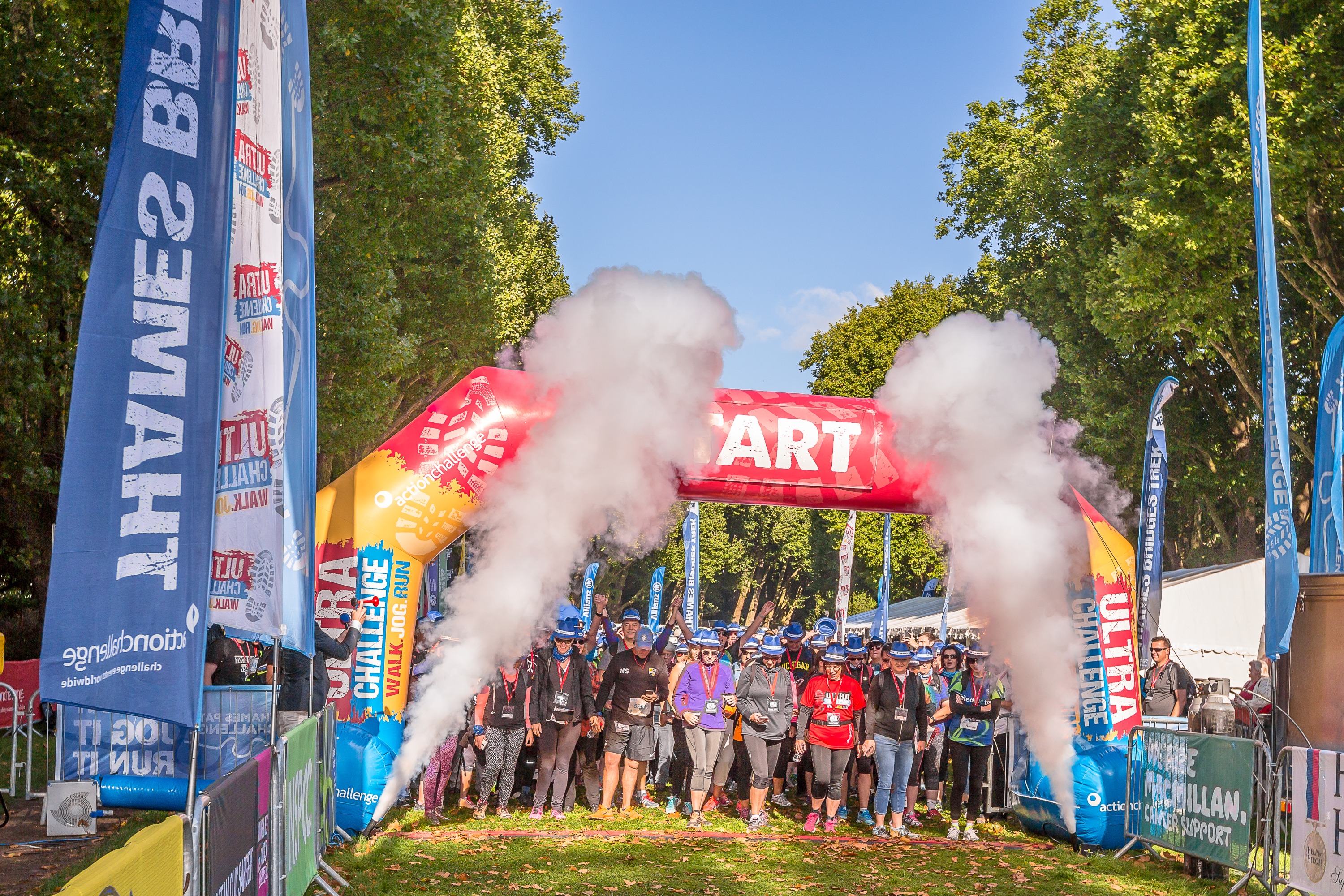 A large group of people outside standing under a large red archway with 'Start' on it. Either side are smoke machines and large flags.