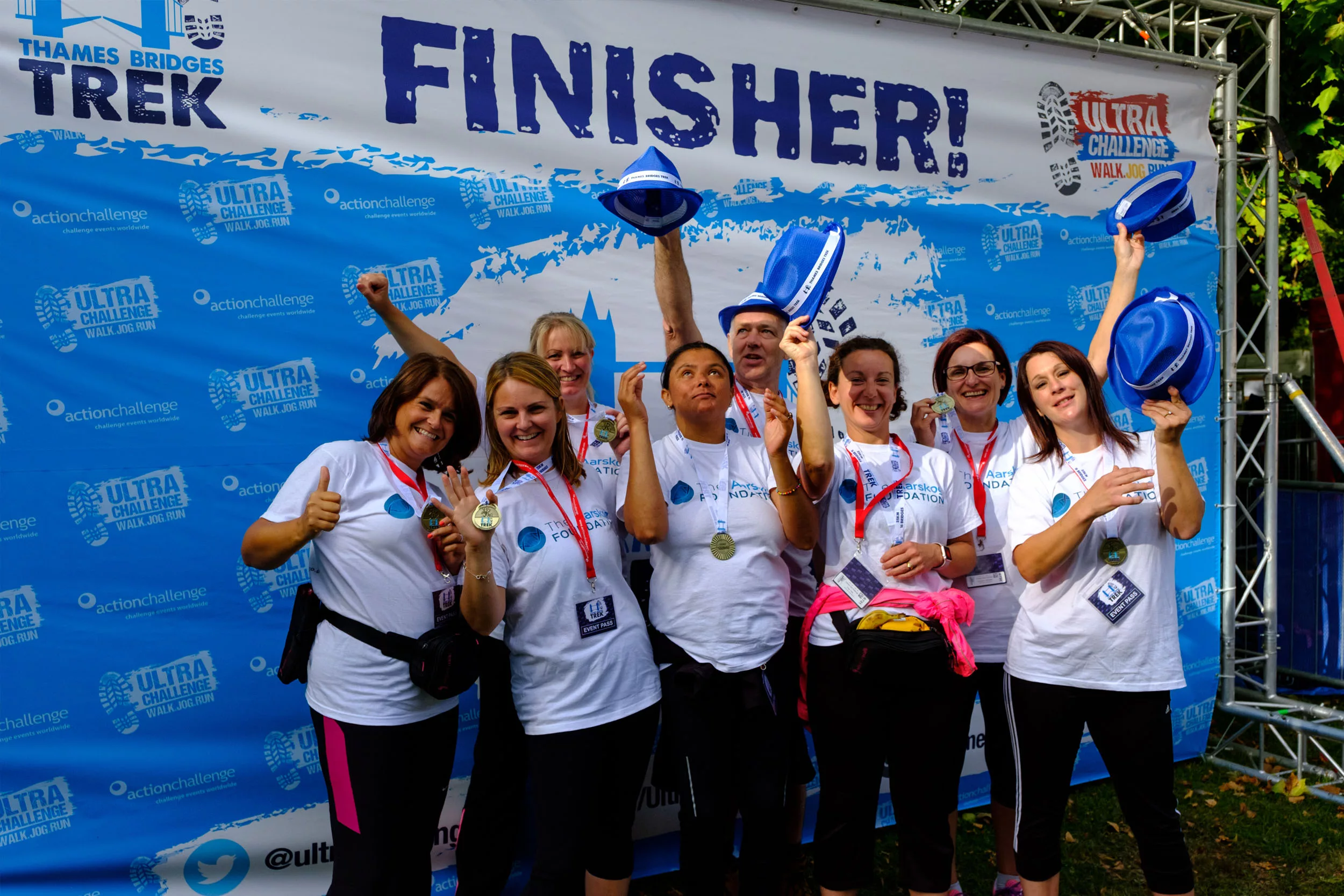 A small group of people celebration in front of a Thames Bridges Trek banner with 'Finisher!' on it.