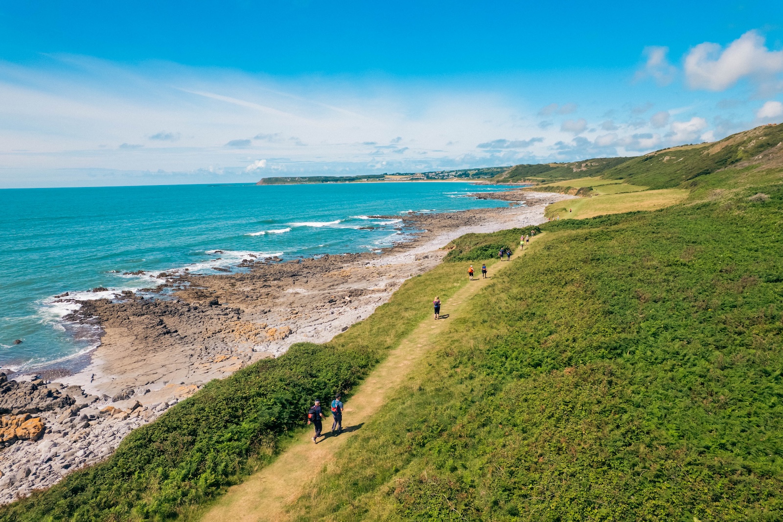 An aerial view of the Gower Peninsula on a sunny day with walkers along the coastal footpath.