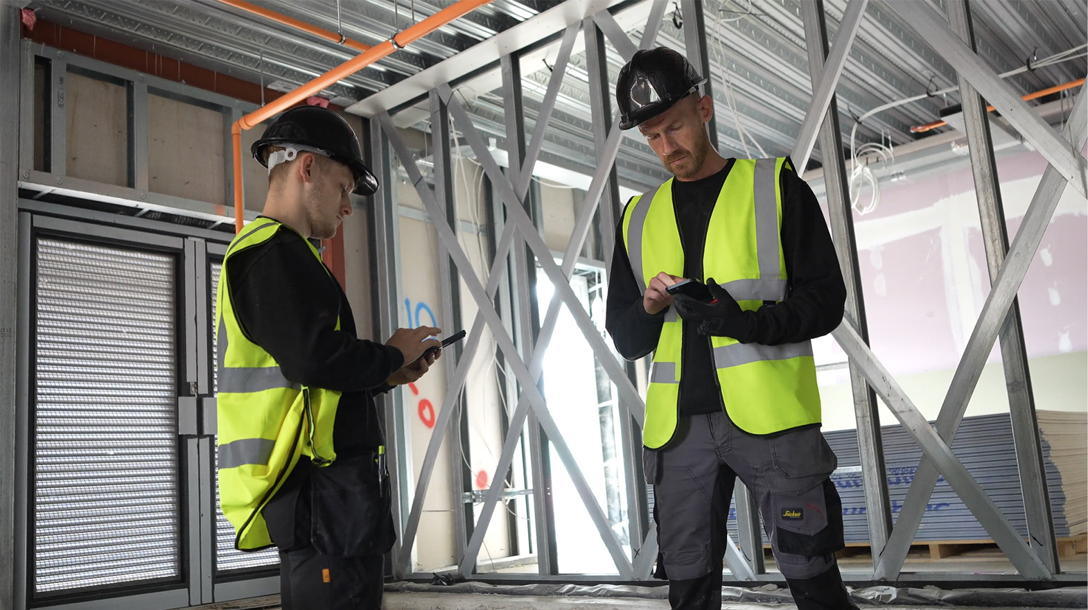 Two construction workers using jobsite management software on their phones to check the project's information on the field.