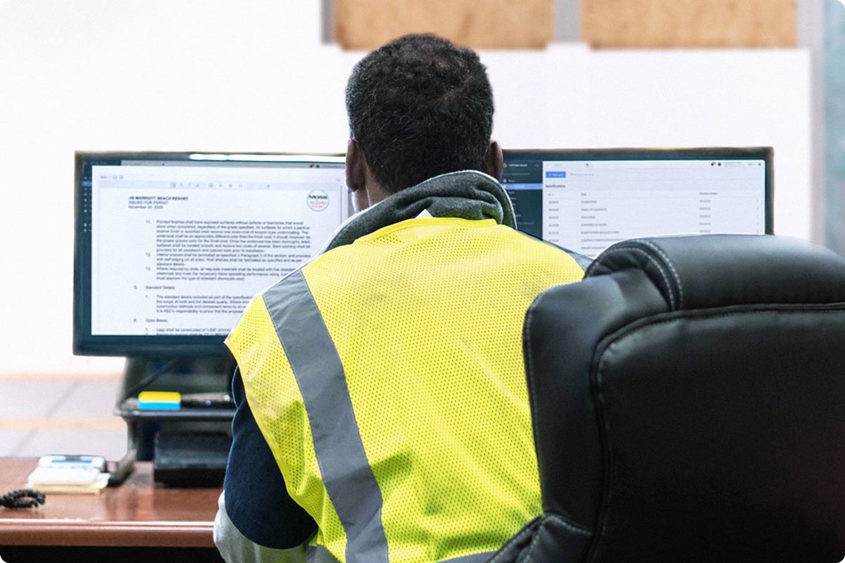 A construction worker is in their trailer looking at documentation for the project. The worker is viewing Fieldwire forms and reports on their computer.
