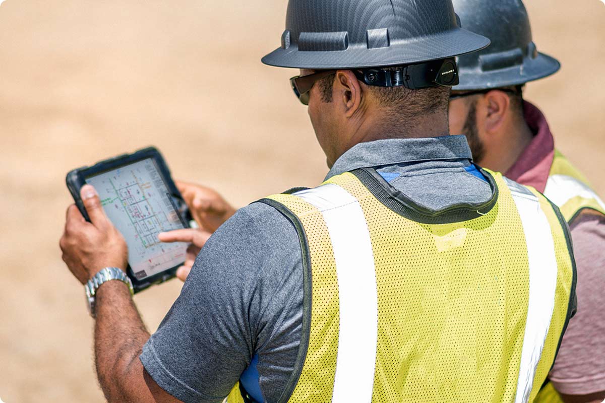 Two construction workers looking at an iPad in the field. They are discussing what the correct task is according to their Fieldwire application.