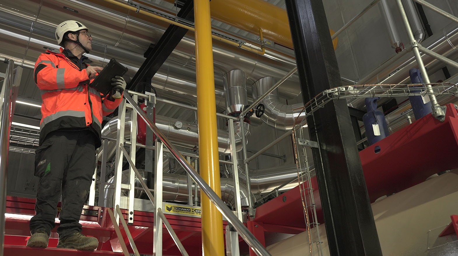 Technician carrying out a technical inspection inside an industrial facility featuring high-performance HVAC systems and pipework networks.