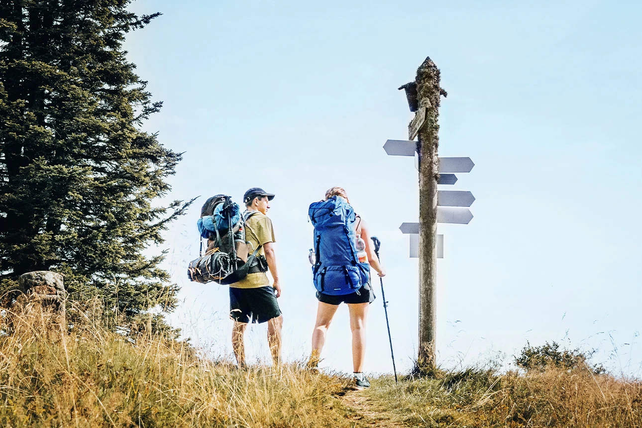 Zwei Wandernde mit Rucksäcken an einem Wegweiser