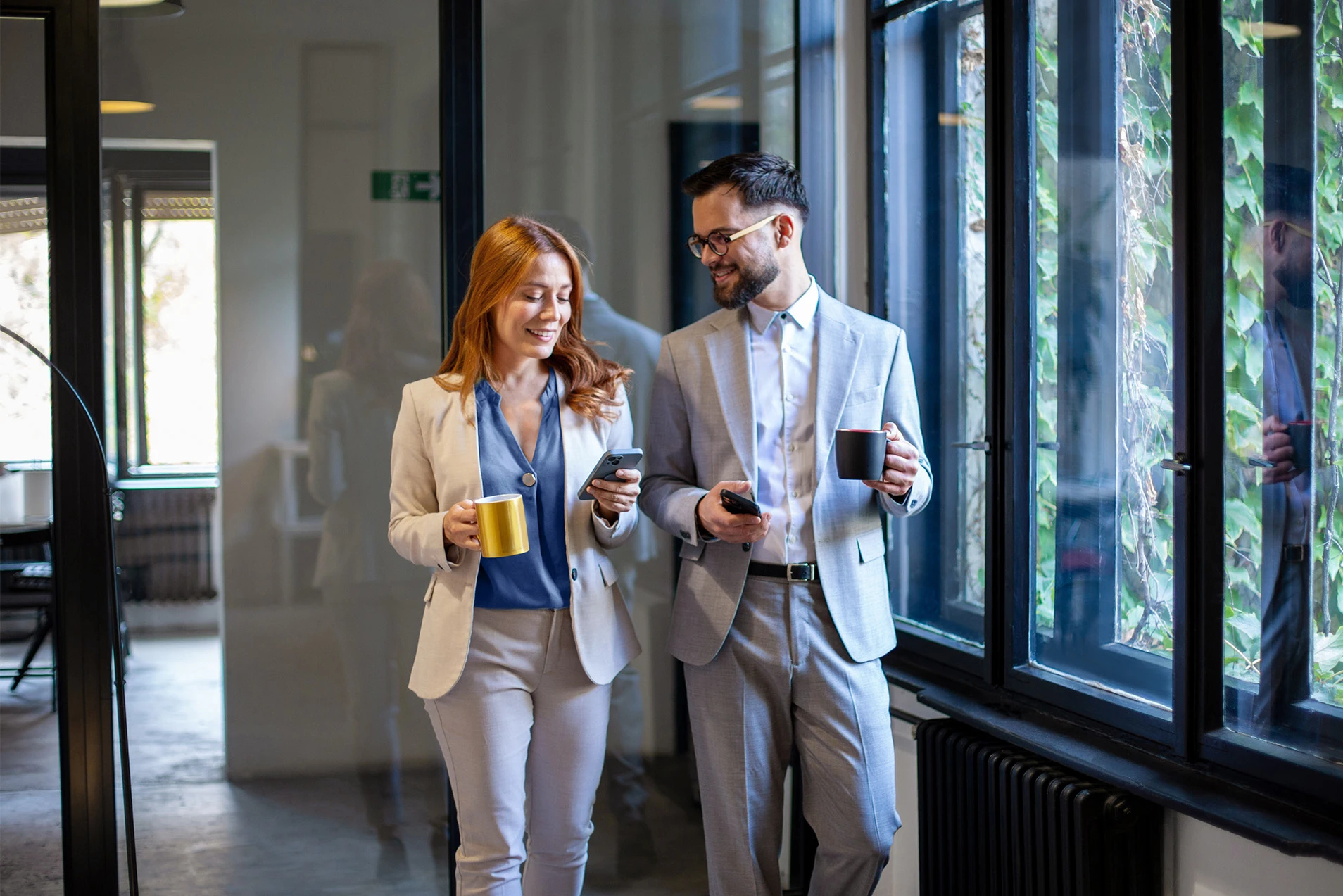 Zwei Personen gehen mit Kaffee durch ein Büro