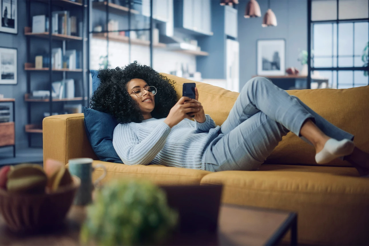 Junge Frau liegend auf Couch mit Handy in der Hand