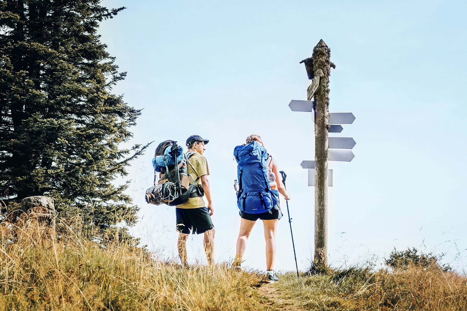 Zwei Wandernde mit Rucksäcken an einem Wegweiser