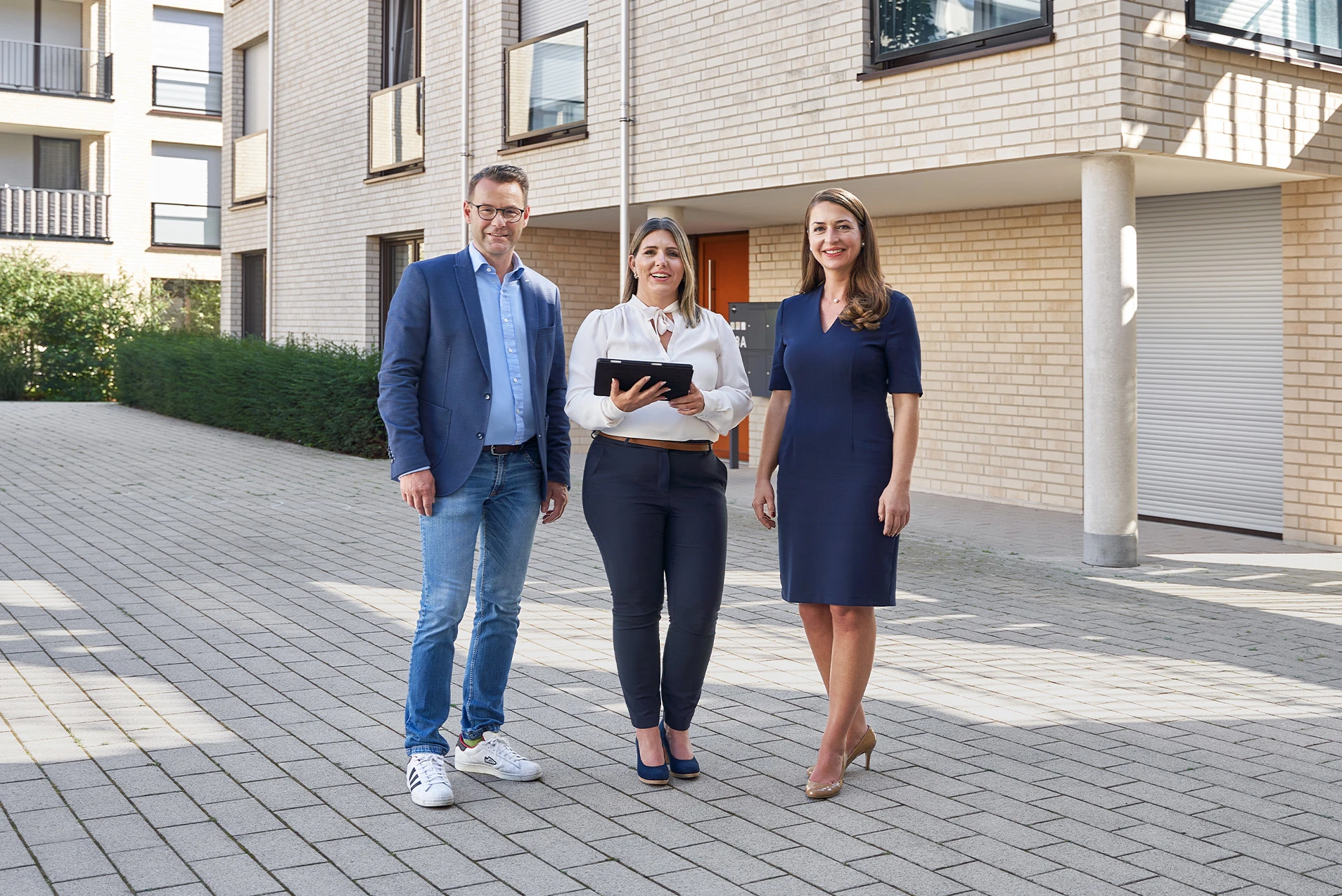 Drei Personen stehen vor einem Gebäude und schauen in die Kamera