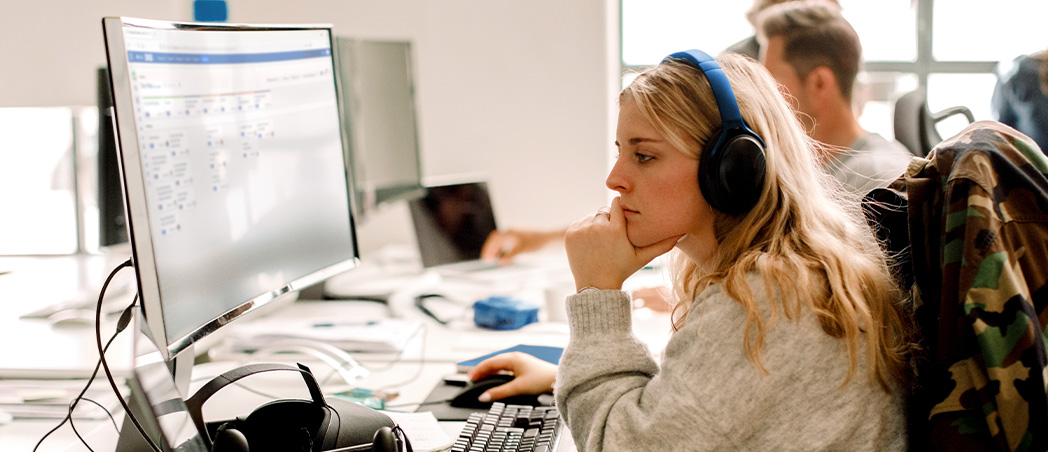 Frau mit Headset arbeitet konzentriert am Computer im Büro