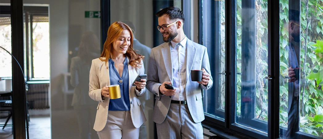 Zwei Personen gehen mit Kaffee durch ein Büro