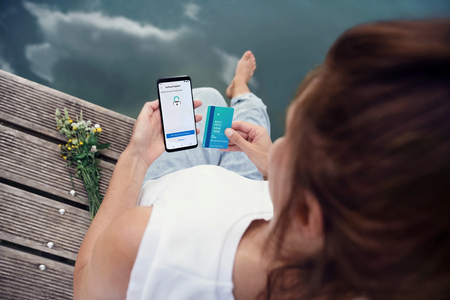 Eine Frau am Wasser mit Smartphone und DKB Debitkarte