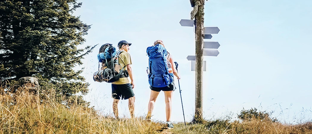 Zwei Wandernde mit Rucksäcken an einem Wegweiser