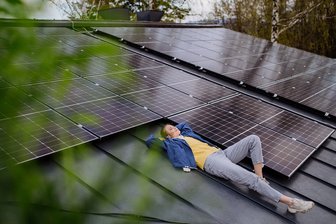 Frau liegt entspannt auf Hausdach neben Solarpanelen