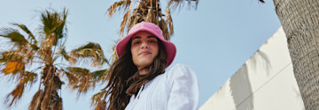 Sommerlicher Look mit weißem Oberteil und auffälligem pinken Hut gegen die Sonne.