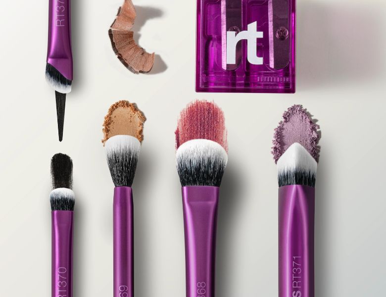 Her ses fem lilla makeupbørster fra Real Techniques på en lysegrå baggrund.