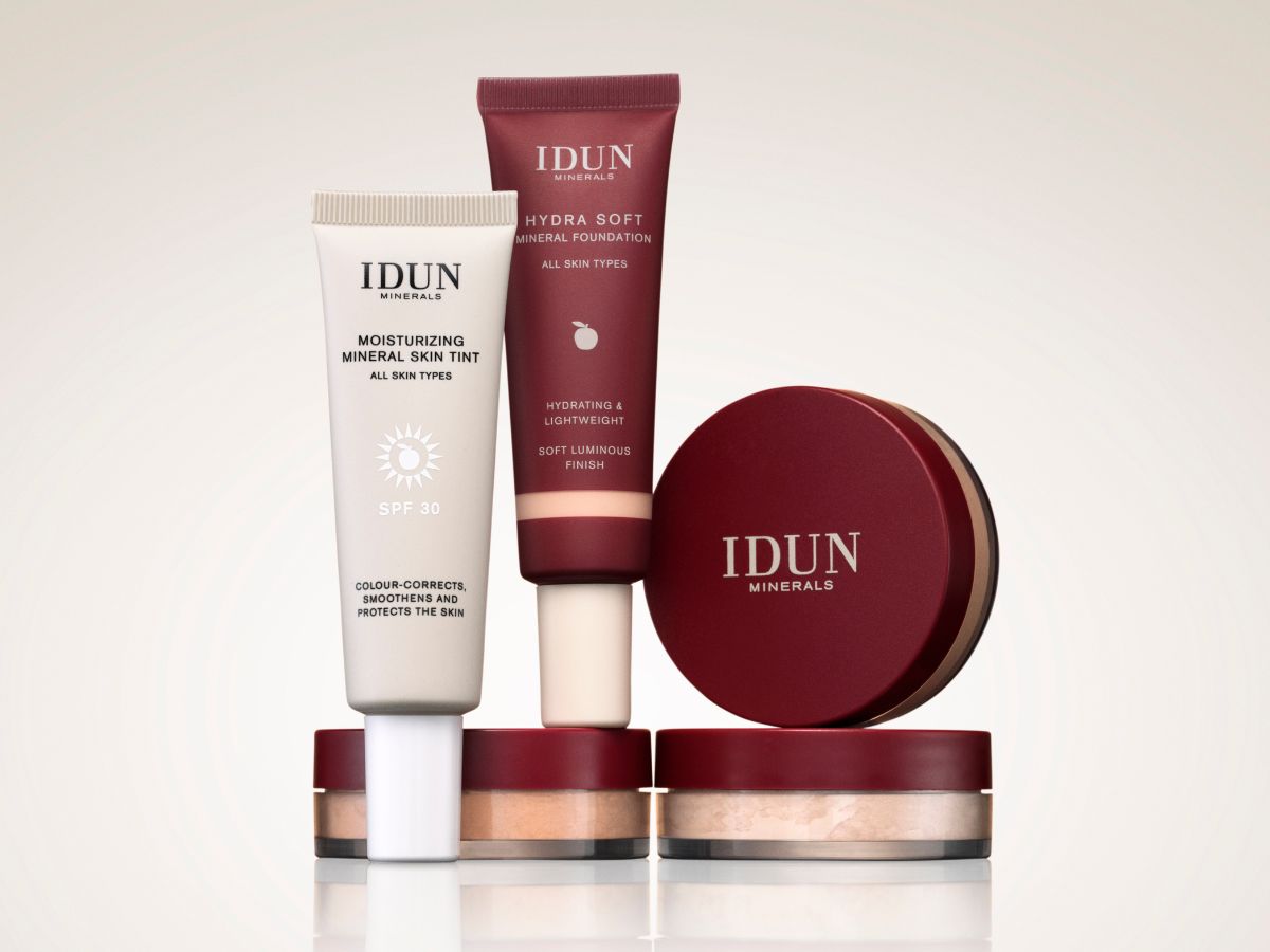 Her ses et billede med makeupprodukter fra IDUN Minerals mod en lys baggrund. Produkterne omfatter blandt andet Moisturizing Mineral Skin Tint SPF 30, Hydra Soft Mineral Foundation, løspudder og en pudderfoundation i bordeauxfarvet emballage. Produkterne er arrangeret samlet med fokus på en naturlig base til ansigtet.