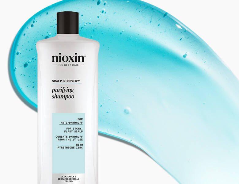 Her ses et billede af en shampoo fra Nioxin placeret mod en lys baggrund med blå gelstruktur bagved. På flasken står teksten “nioxin PRO CLINICAL SCALP RECOVERY purifying shampoo”. Produktet er udviklet til skæl og tør, irriteret hovedbund.