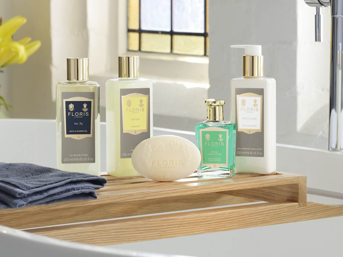 Floris London kropsplejeprodukter står samlet på en træbakke ved en vask, herunder shower gel, håndcreme, sæbe og parfume i elegante flasker.