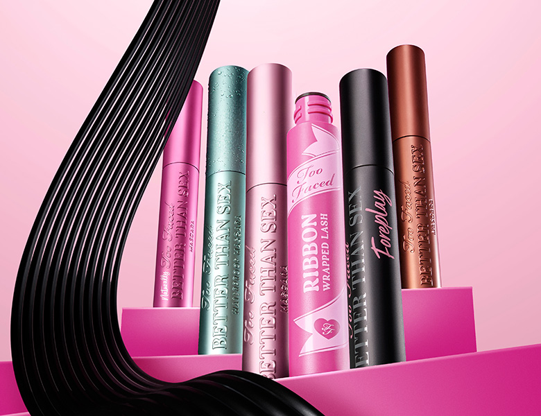 Her ses et billede med flere mascaraprodukter fra Too Faced placeret mod en pink baggrund. På produkterne står blandt andet “Better Than Sex” og “Ribbon Wrapped Lash”.