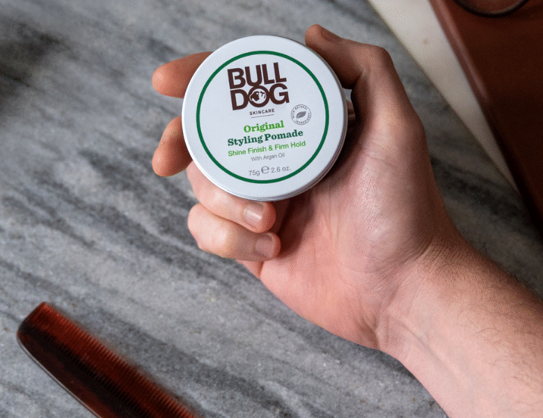 Her ses en hånd, som holder et Bulldog produkt i hånden. Baggrunden er et gråt stenbord, hvor der ses en kam.