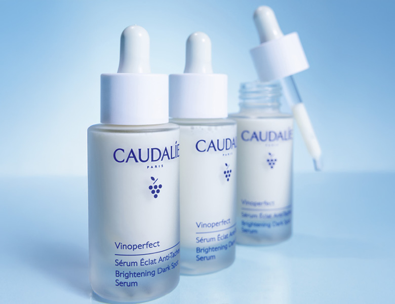 Her ses CAUDALIE serummer i glasflasker med pipette på en blå baggrund.