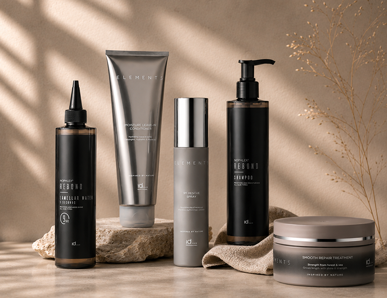 Her ses et billede med hårplejeprodukter fra IdHAIR placeret på sten mod en varm, beige baggrund. Produkterne kommer blandt andet fra serierne “Elements” og “Noplex Rebond” og omfatter shampoo, conditioner, treatment og spray.