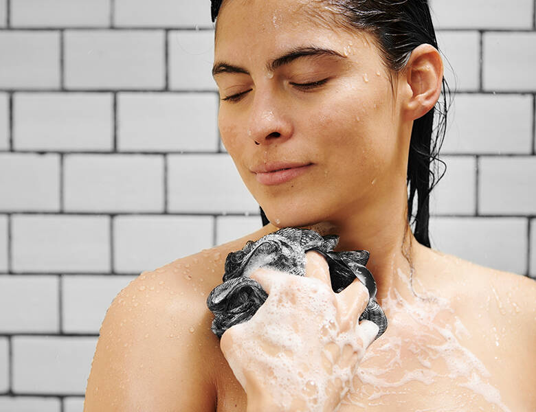 Her ses en kvinde i badet. Hun holder en loofah med sæbe op foran sig.