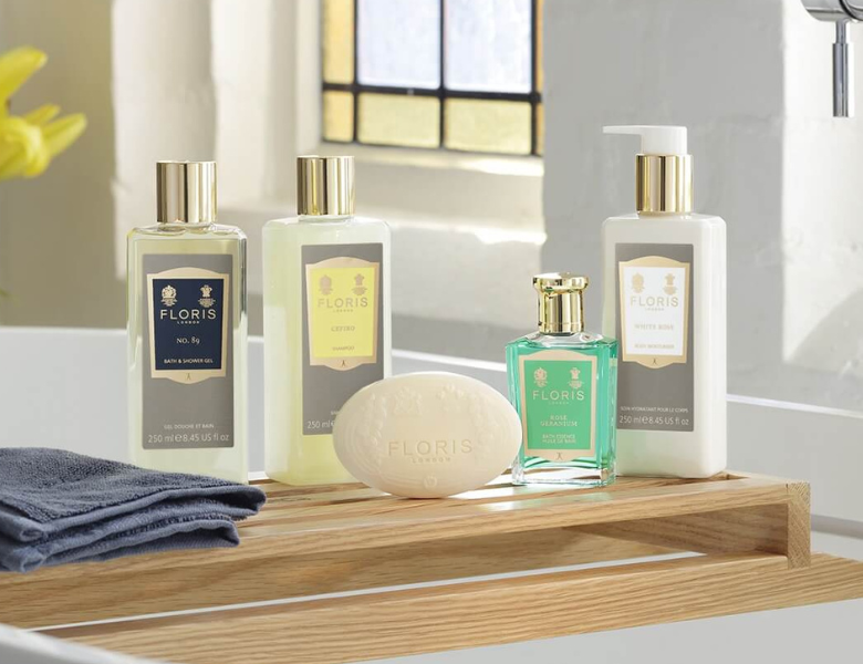 Floris London kropsplejeprodukter står samlet på en træbakke ved en vask, herunder shower gel, håndcreme, sæbe og parfume i elegante flasker.