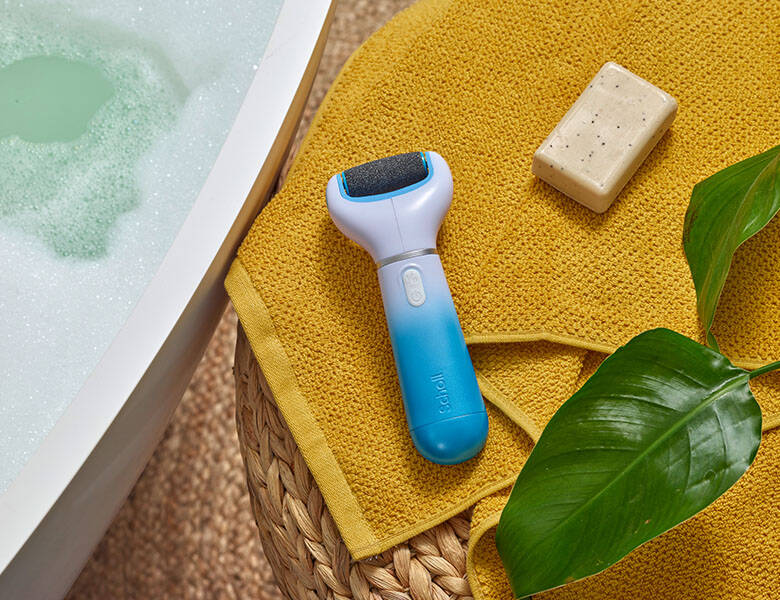 Her ses en balje med vand, et gult håndklæde, og to Scholl produkter.