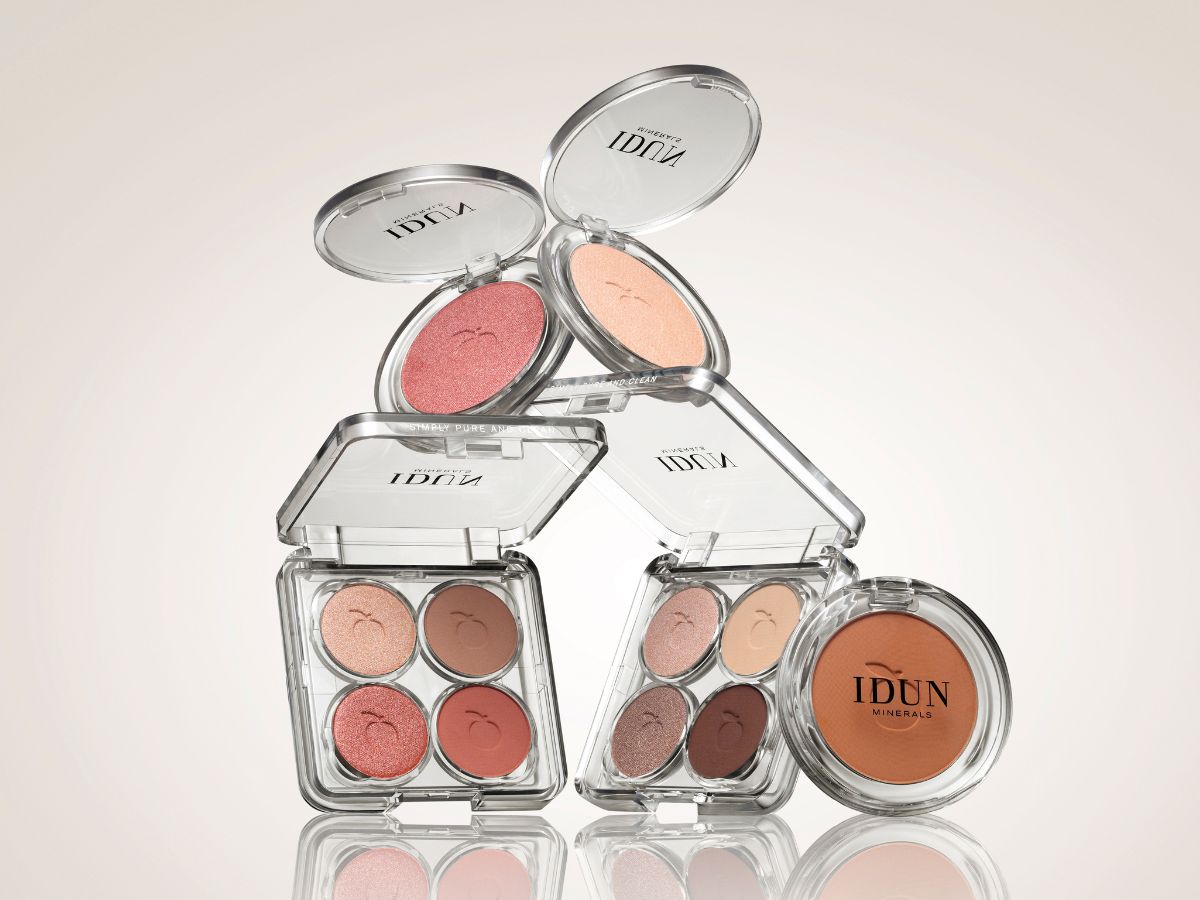 Her ses et billede med øjenmakeup fra IDUN Minerals mod en lys baggrund. Produkterne omfatter to åbne øjenskyggepaletter med fire nuancer hver, to åbne single eyeshadows og en bronzer eller pudder. De gennemsigtige etuier gør farverne synlige og fremhæver de varme, naturlige nuancer.