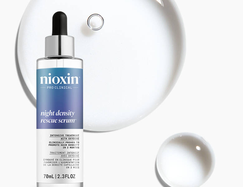 Her ses et billede af et hårserum fra Nioxin placeret mod en lys baggrund med gennemsigtige dråbeformer. På flasken står teksten “nioxin PRO CLINICAL night density rescue serum”. Produktet har pipette og blå detaljer på etiketten.