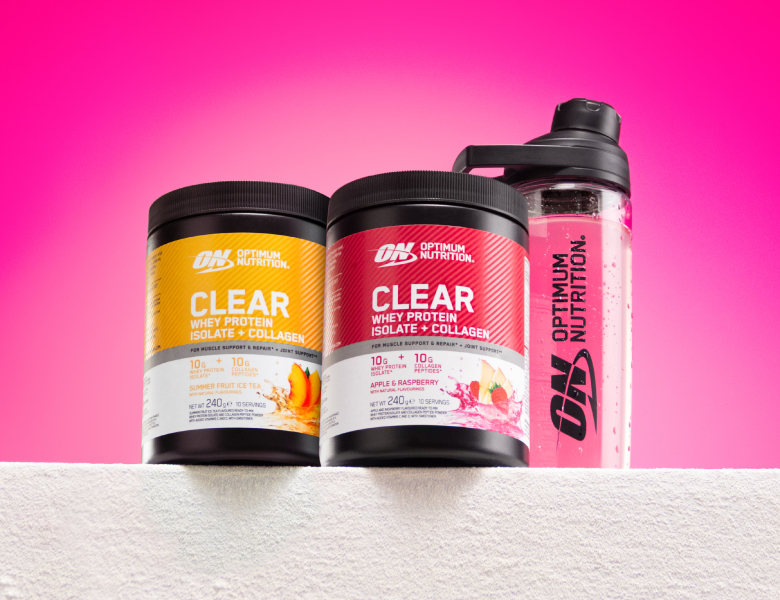 To bøtter Optimum Nutrition Clear Whey Protein Isolate med collagen og en gennemsigtig drikkedunk står på et hvidt håndklæde foran en pink baggrund.