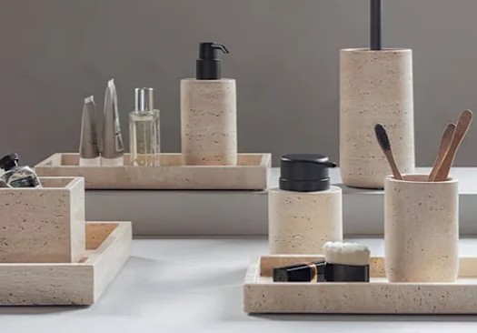 Beige badeværelsestilbehør i steninspireret design med sæbedispenser, tandkrus, bakker og beholdere arrangeret ved et spejl.