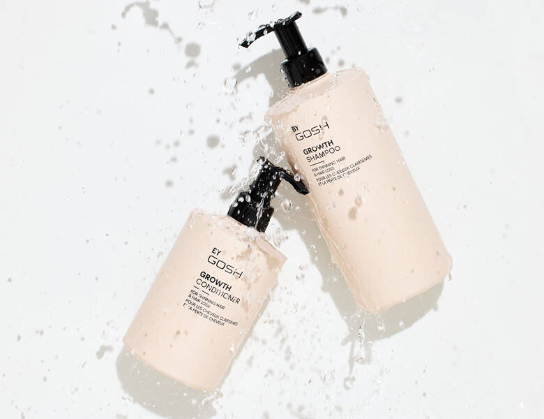Her ses en sart lyserød shampoo og balsam fra Gosh. Baggrunden er hvid og der falder vand ned på produkterne.