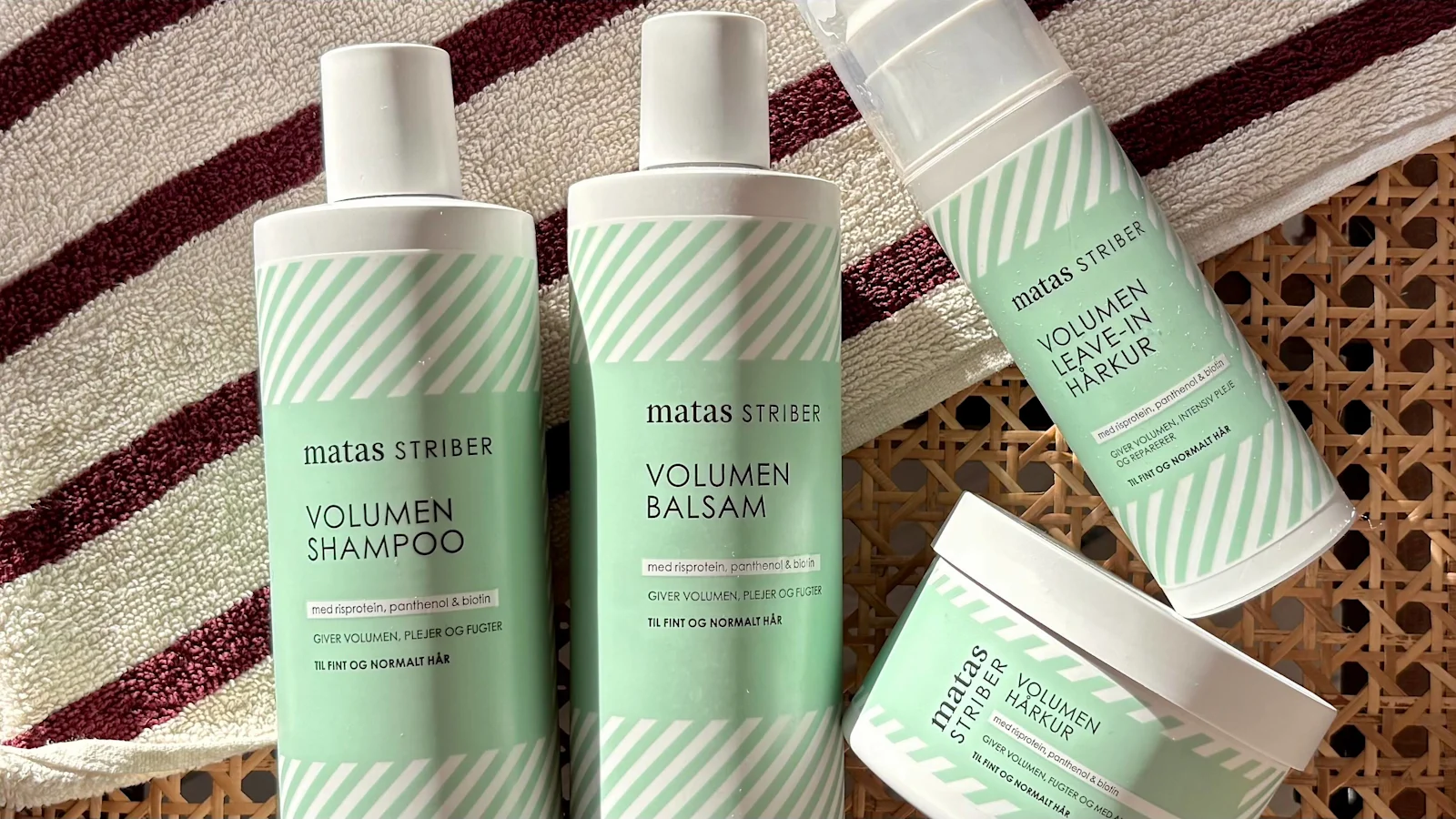 Her ses Matas Striber Volumen Shampoo, Volumen Balsam, Volumen Leave-in Hårkur og Volumen Hårkur på et vævet underlag med et stribet håndklæde i baggrunden.