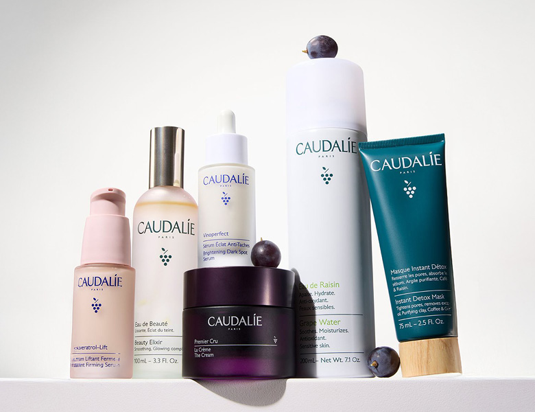 Her ses CAUDALIE hudplejeprodukter – serum, creme og mist i forskellige flasker på en lys baggrund.