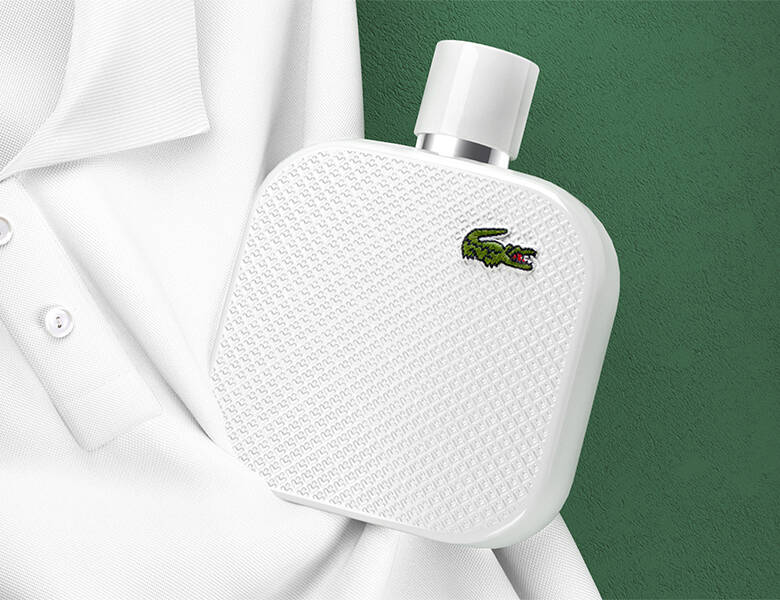 Her ses en hvid polo på en grøn baggrund. Derpå ligger en hvid Lacoste parfume.