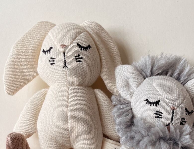 To dekorative produkter til børn: en grå strikket løvebamse og en cremefarvet tandformet taske med ansigt og brune hanke.