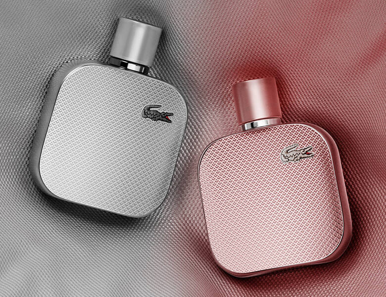 Her ses en sølv og lyserød baggrund med to Lacoste parfumer - en i sølv og en i lyserød.