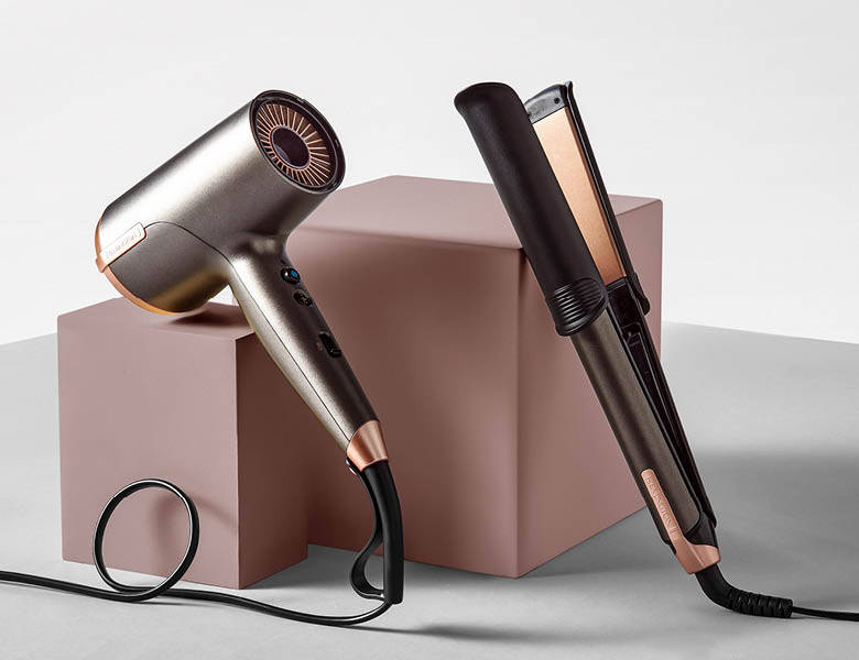 Her ses en hårtørre og et glattejern, som står op af en lyserød kasse på en hvid baggrund.