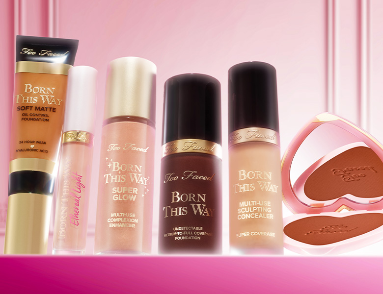 Her ses et billede med forskellige ansigtsprodukter fra Too Faced placeret mod en pink baggrund. På produkterne står blandt andet “Born This Way”, og der ses foundation, concealer og bronzer.