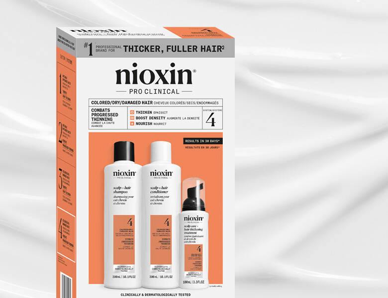 Her ses et billede af et hårplejekit fra Nioxin placeret mod en lys baggrund. På æsken står teksten “nioxin PRO CLINICAL” samt “THICKER, FULLER HAIR”. Sættet indeholder shampoo, conditioner og treatment-produkter.