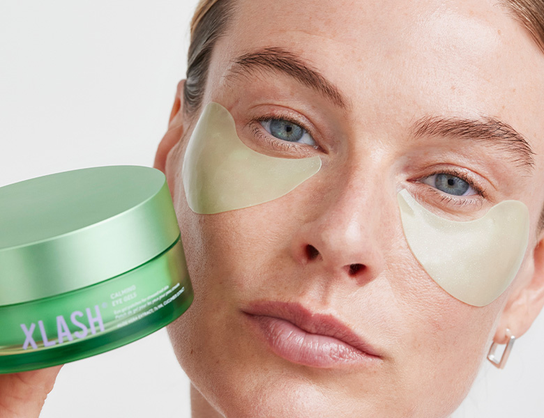 Her ses en person med øjenmasker under øjnene, der holder Xlash øjenmasker.